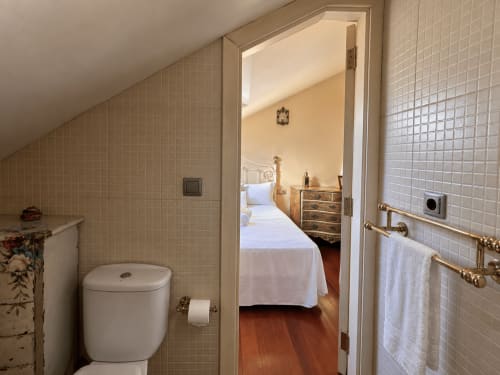 Baño moderno con azulejos blancos, inodoro y toallero que conecta con el dormitorio del apartamento Lembrare en Baiona