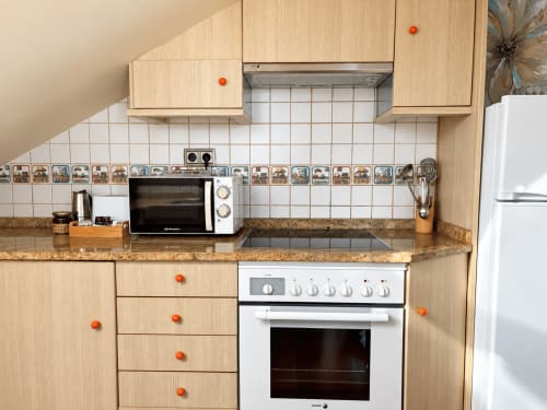 Cocina moderna en apartamento de Baiona con muebles de madera clara, azulejos blancos, microondas y horno