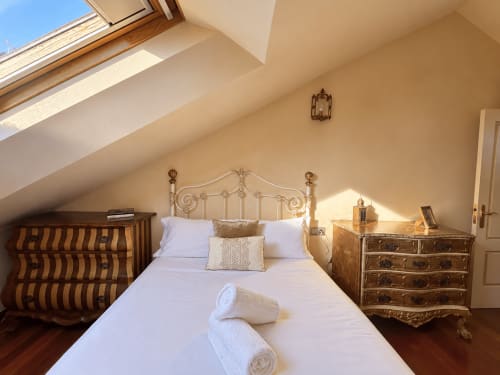 Elegante habitación bajo techo en Baiona con cama de metal ornamentada, mobiliario de madera, claraboya y vistas al mar
