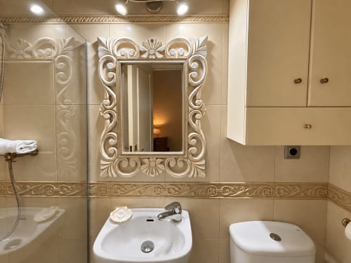 Baño elegante del apartamento Holibai en Baiona con espejo ornamental, lavabo blanco y paredes de azulejos beige