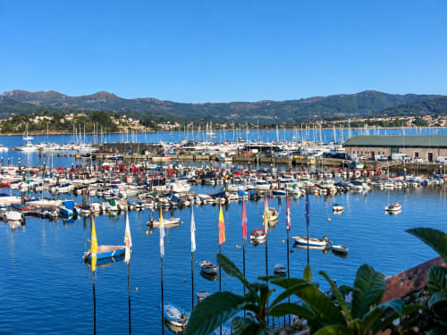 Marina de Baiona con velas coloridas, paseo marítimo y montañas, vista al mar desde el apartamento Lembrare