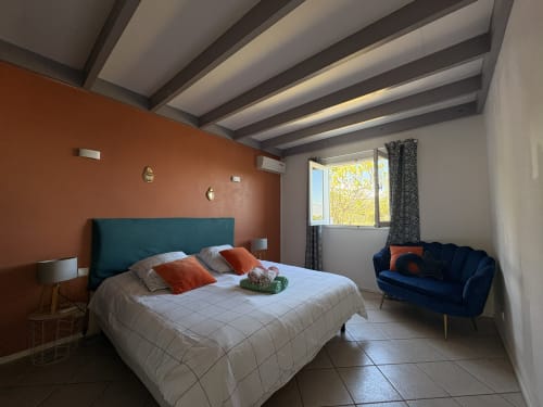 Spacious villa bedroom at La Villa Maraloupia with teal headboard, orange accent wall, and sea view in Les Avirons, Réunion