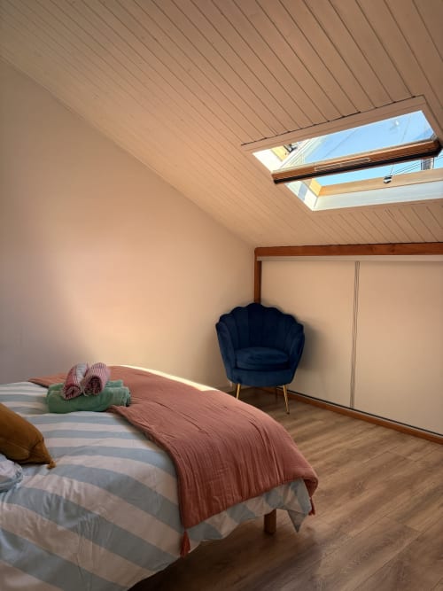 Modern bedroom with skylight at La Villa Maraloupia villa in Les Avirons, featuring bed with pink throw, blue armchair, and