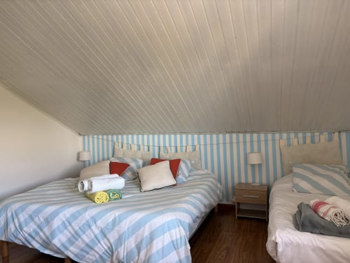 Bright villa bedroom with blue striped bedding, sloped ceiling, and multiple beds at La Villa Maraloupia in Les Avirons
