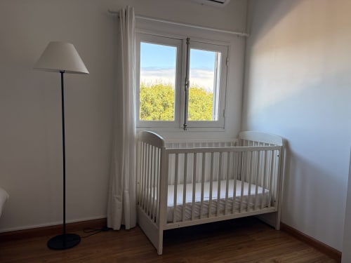 Bright nursery room at La Villa Maraloupia in Les Avirons with white crib, floor lamp, and ocean view through large windows