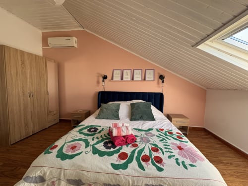 Cozy attic bedroom at La Villa Maraloupia with peach walls, floral quilt, dark headboard, AC unit, and skylight in Les