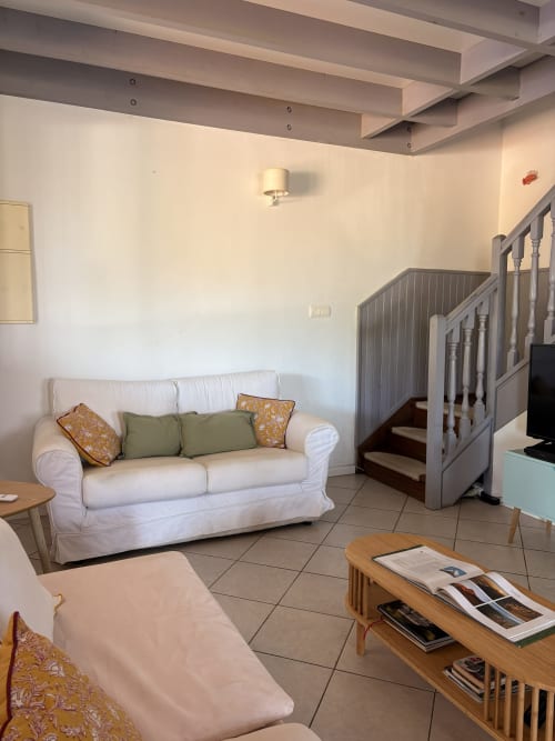 Modern villa living room with white sofa, wooden beams ceiling, and staircase at La Villa Maraloupia, Les Avirons