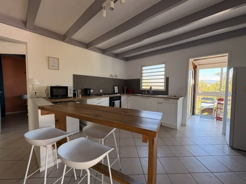 Modern kitchen with dining table, white chairs, sea view from balcony door at La Villa Maraloupia, Les Avirons
