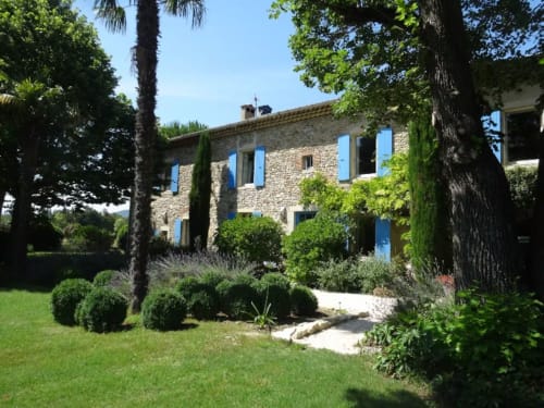 Maison de pierre avec volets bleus entourée de jardins entretenus et palmiers aux Buis de Fontjuliane à Sauzet