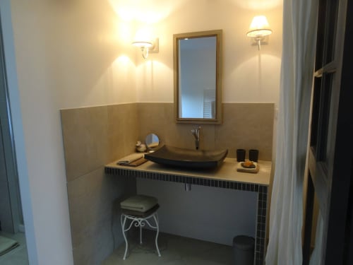 Salle de bain élégante aux Buis de Fontjuliane avec vasque noire, miroir encadré, éclairage ambiant et tabouret de toilette