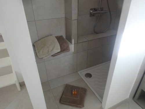 Douche spacieuse à carrelage gris avec niche intégrée, serviettes de toilette et pomme de douche pluie aux Buis de