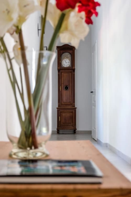 Élégante horloge de parquet dans le couloir lumineux des Buis de Fontjuliane à Sauzet, avec des fleurs fraîches à proximité