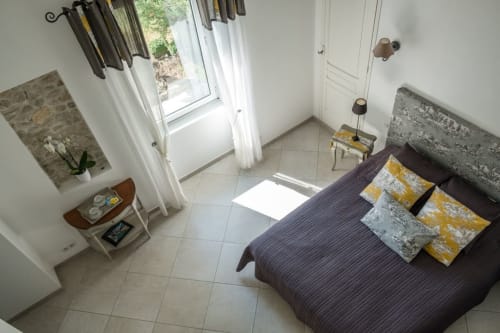 Chambre lumineuse aux Buis de Fontjuliane avec lit sombre, oreillers jaunes, vue sur Sauzet