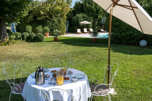 Table de petit-déjeuner en terrasse au jardin des Buis de Fontjuliane, Sauzet, avec piscine et transats en arrière-plan
