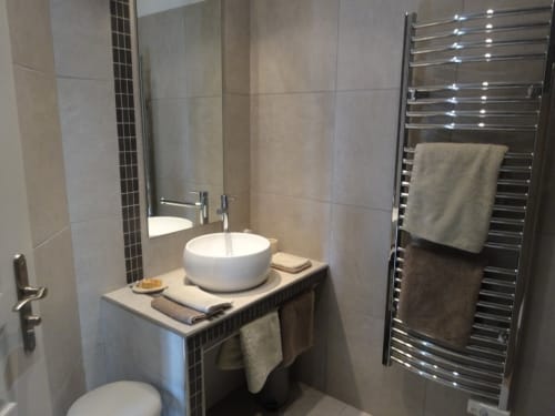 Salle de bain moderne aux Buis de Fontjuliane à Sauzet avec vasque ronde blanche, sèche-serviettes chauffant et murs en carrelage neutre