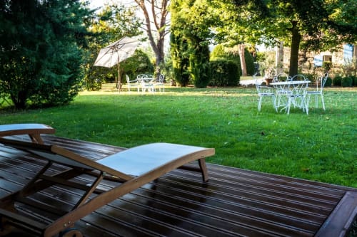 Jardin ensoleillé aux Buis de Fontjuliane à Sauzet avec transats, tables de repas, parasol et pelouse verdoyante