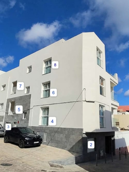 Moderno edificio blanco Edificio Maron en Morro Jable con unidades numeradas, SUV negro estacionado, cielo azul