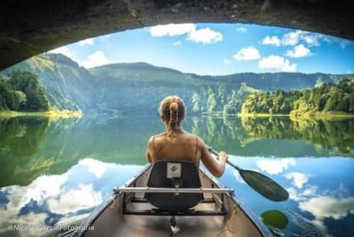 Woman kayaking on serene mirror lake surrounded by forested mountains, Ribeirinha Portugal adventure experience