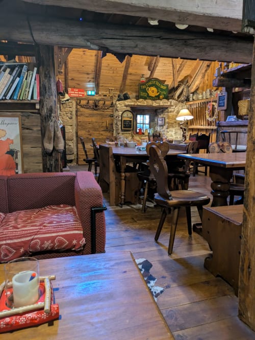 Intérieur rustique du lodge Gite Du Bois De L'ours à Orcières avec foyer en pierre, tables à manger et sièges rouges