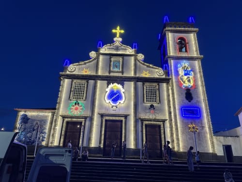 Illuminated church facade at night in Ribeirinha, Portugal, with neon religious decorations and blue lights