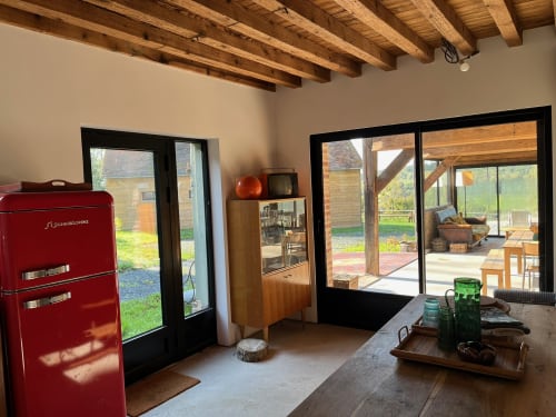Intérieur de villa moderne au Domaine de Blanvatel avec poutres apparentes, réfrigérateur vintage rouge et portes vitrées sur les jardins