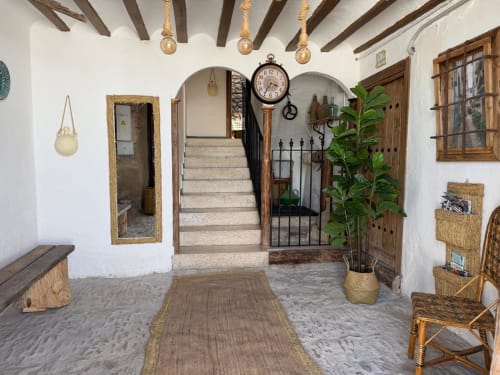 Entrada rústica de Casa de la Aguadora en Iznatoraf: escaleras de piedra, vigas de madera, reloj vintage y decoración española tradicional