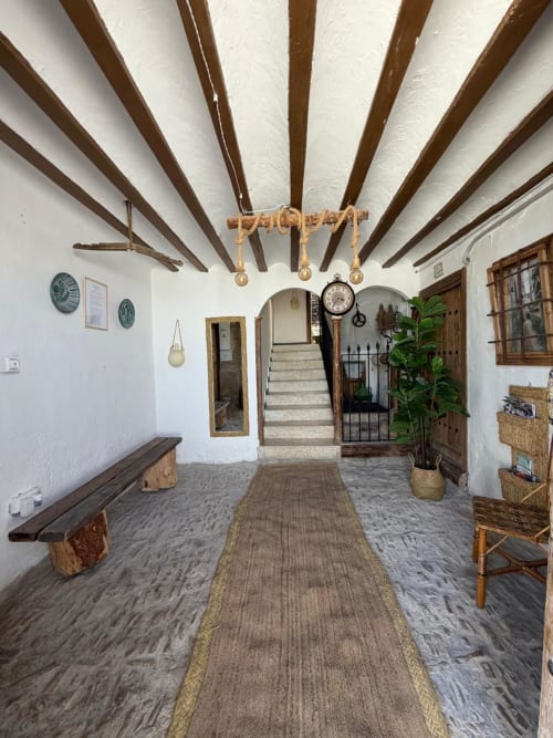Entrada de cabaña rústica española con vigas de madera vista, paredes blancas y decoración tradicional en Casa de la Aguadora
