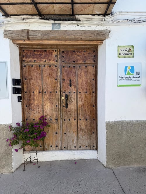 Entrada con puerta rústica de madera de la casita Casa de la Aguadora en Iznatoraf, decorada con flores de buganvilea morada