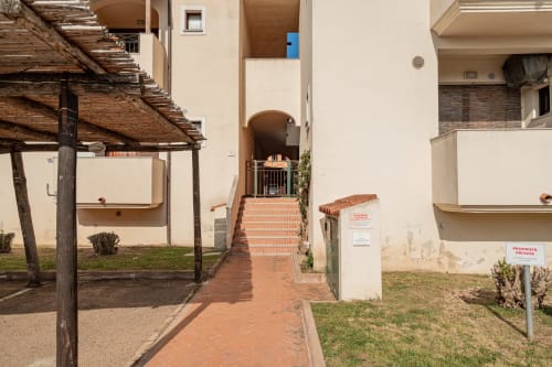 Brick pathway entrance to Short Let's Olbia property with white buildings, pergola, and private property signage in Olbia,