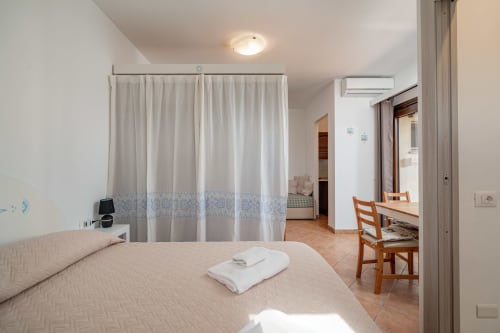 Spacious hotel room at Short Let's Olbia with bed, curtain divider, wooden chair, and terracotta tiles