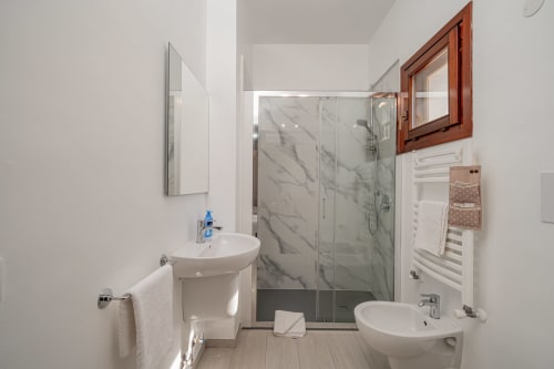 Modern bathroom at Short Let's Olbia with marble shower, pedestal sink, bidet, and wooden window frame.