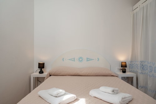 Bright bedroom at Short Let's Olbia with white headboard, twin beds, beige bedding, nightstands with lamps, and sheer