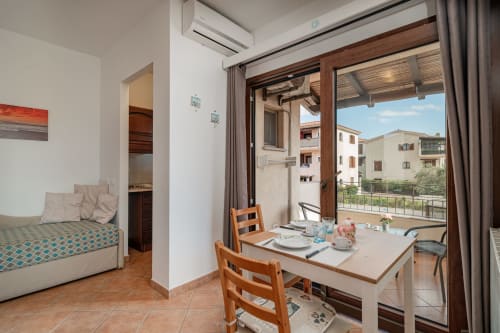 Bright apartment interior at Short Let's Olbia with dining table, bedroom, and balcony overlooking Olbia buildings