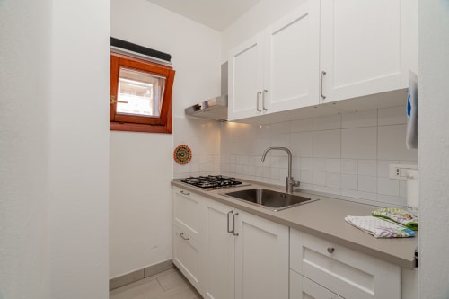 Modern white kitchen with gas stove, sink, and wooden-framed window at Short Let's Olbia apartment in Italy
