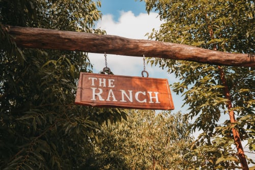 Placa 'The Ranch' pendurada em viga de madeira rústica cercada por vegetação exuberante no hotel The Ranch Project em Gonçalves, Brasil