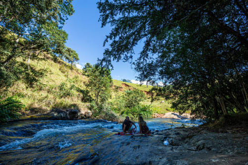 Duas pessoas vadiam em um rio azul pristino cercado por floresta exuberante e morros verdes no The Ranch Project em Gonçalves, Brasil