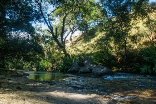 Tranquilo riacho cercado por densa floresta e formações rochosas na villa The Ranch Project.Co em Gonçalves.
