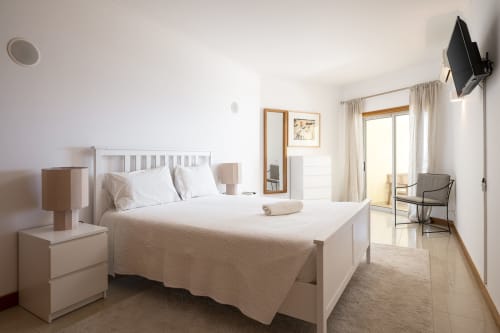 Bright bedroom at RB Algarve Vilamoura with white bed, modern furnishings, flat-screen TV, and balcony access