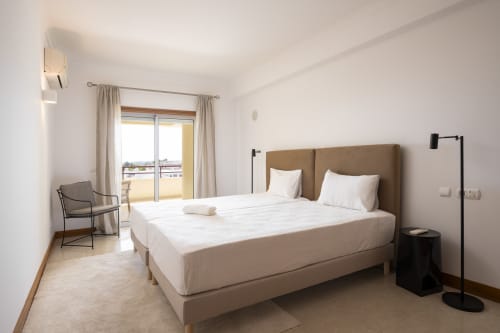 Modern bedroom at RB Algarve Vilamoura apartment with tan headboard, balcony view, and contemporary furnishings
