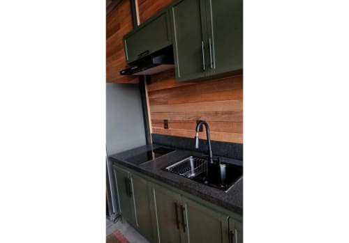 Cozinha moderna com armários verde oliva, bancada em granito preto e painel de madeira no Nordic Tree Cabin da The Ranch