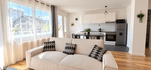 Apartamento moderno de planta abierta en NN Patrimoine en Annemasse con sofá crema, cocina equipada y vistas a la ciudad desde el balcón