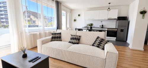 Sala de estar moderna de apartamento urbano con sofá crema, acentos negros, cocina abierta y vistas a la ciudad en NN Patrimoine
