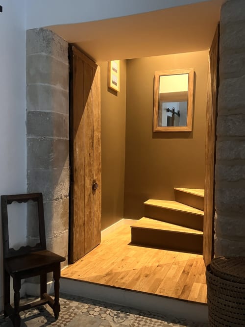 Entrée de chambre chaleureusement éclairée aux anciennes écuries du Château avec porte en bois, miroir, murs en pierre et parquet
