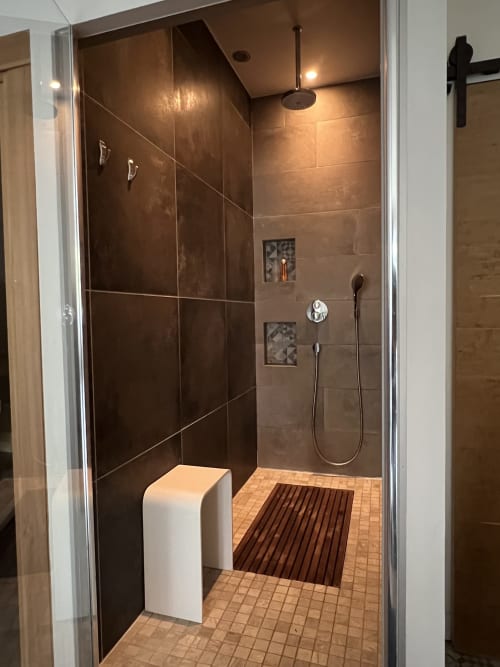Salle de douche à l'italienne aux murs en carrelage sombre, pomme de douche pluie et partie du sol en bois aux Anciennes écuries du Château