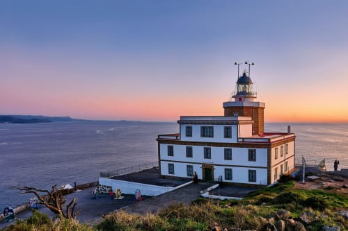Albergue A Casa do Boi al atardecer con torre faro frente al mar en Covas, Ames, ES