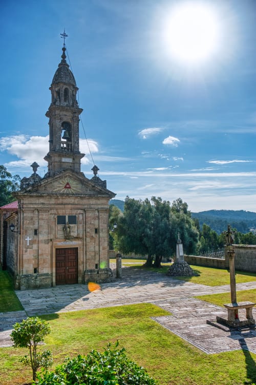 Capilla de piedra con campanario en el albergue A Casa do Boi en Covas, Ames, Galicia, rodeada de exuberantes jardines
