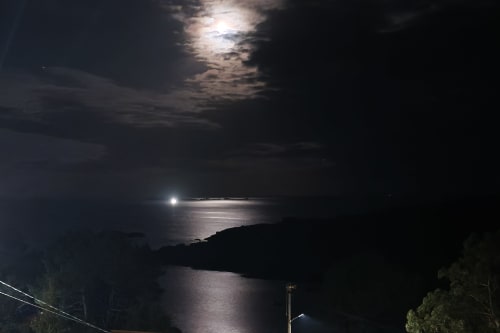 Vista nocturna iluminada por la luna de la costa de Cee con luna llena brillante reflejada en el agua, costa rocosa recortada en A Ballenera de