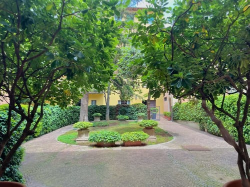 Rigoglioso cortile con giardino a Living Palazzi Storici Bologna, sentieri alberati e edificio storico in giallo