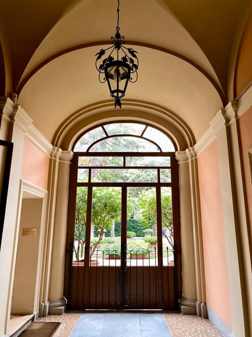 Elegante corridoio con volta a botte nel palazzo storico di Bologna, con lampadario ornato, soffitto ad archi e vista sul giardino