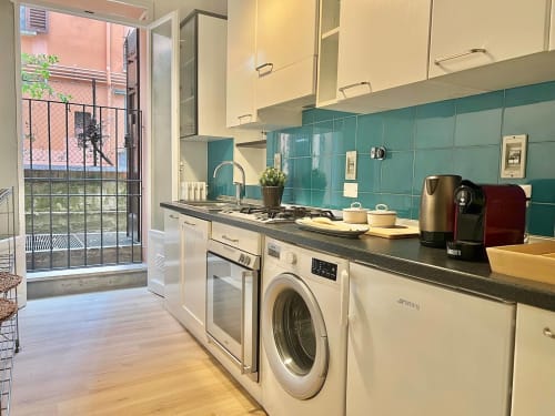 Cucina moderna con piastrelle turchesi, armadi crema e porta-finestra con vista sul giardino - Living Palazzi Storici Bologna